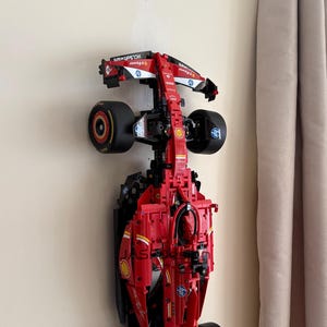 May include: A red and black Lego Ferrari Formula 1 race car model is mounted on a wall. The car has the logos for Shell, HP, and Scuderia Ferrari.