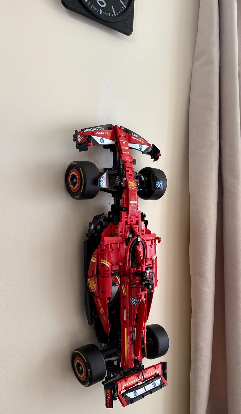 May include: A red and black Lego Ferrari Formula 1 race car model is mounted on a wall. The car has the logos for Shell, HP, and Scuderia Ferrari.