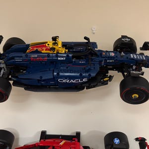 May include: A blue and yellow Lego Formula 1 race car with the Oracle and Red Bull logos. The car is on a white wall.