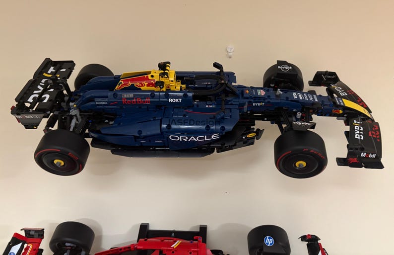 May include: A blue and yellow Lego Formula 1 race car with the Oracle and Red Bull logos. The car is on a white wall.
