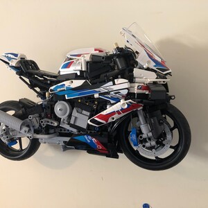 May include: A white, blue and red Lego motorcycle model with a clear windscreen. The motorcycle has a detailed engine and wheels.
