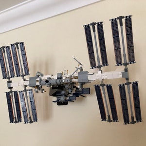 May include: A white and gray Lego model of the International Space Station with solar panels, a central module, and robotic arms.