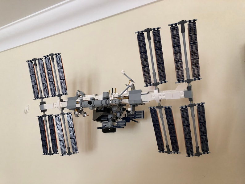 May include: A white and gray Lego model of the International Space Station with solar panels, a central module, and robotic arms.