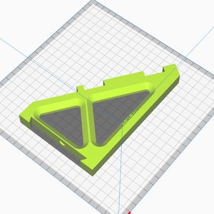 May include: A bright lime green 3D-printed object with a geometric design. The object features two triangular cutouts and a rectangular base. The design includes a small circular hole and text on the side. The object is set against a grid background.