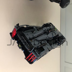 Pu&ograve; includere: Un modello di auto Peugeot in Lego nero e grigio con accenti rossi e blu. L'auto &egrave; sospesa in aria, rivolta verso la fotocamera.