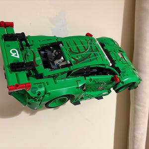May include: A green toy car made of interlocking plastic bricks. The car has a detailed design with red accents and the number 9 in white. The car's hood features a brown and green pattern.