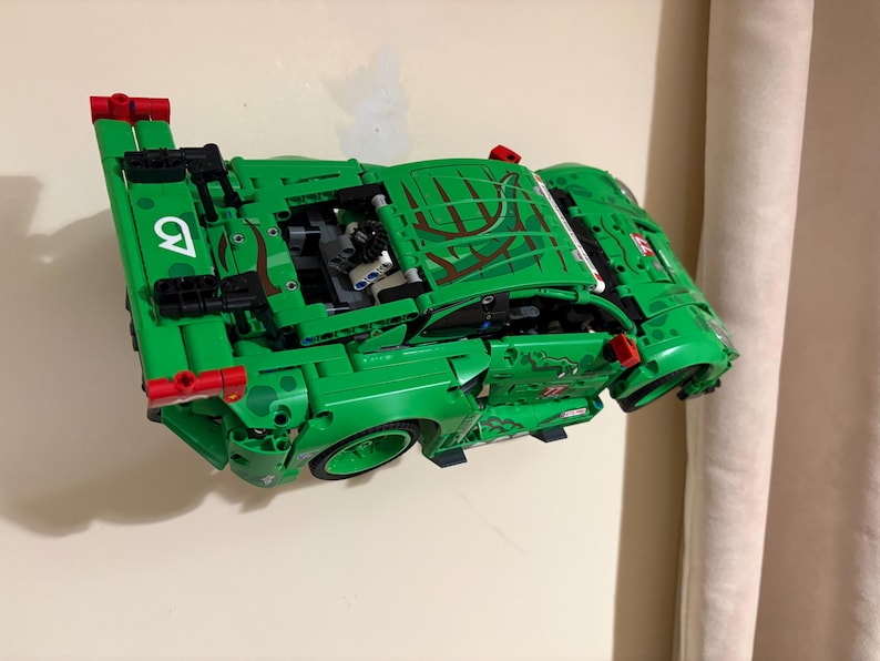 May include: A green toy car made of interlocking plastic bricks. The car has a detailed design with red accents and the number 9 in white. The car's hood features a brown and green pattern.