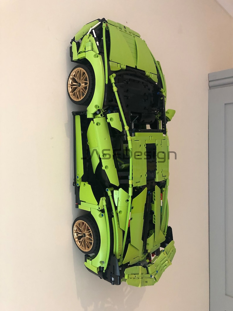 May include: A green Lego model of a sports car, mounted on a wall. The car has black accents and gold wheels.