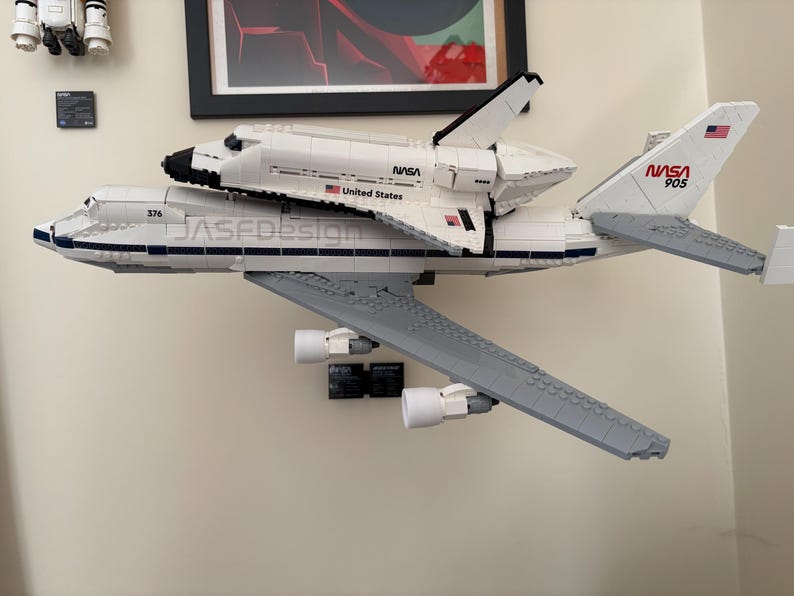 May include: A white and gray LEGO model of a NASA space shuttle mounted on top of a Boeing 747. The model has the NASA logo and the text "United States" on the side. The tail of the plane has the number "905" and a US flag.