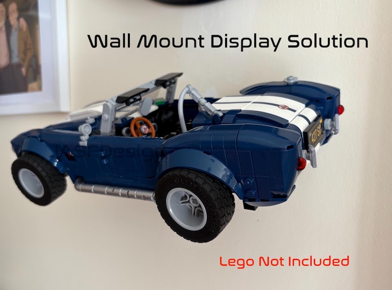 Op de afbeelding: Een blauwe speelgoedauto met witte racestrepen is aan de muur bevestigd. De auto heeft zwarte banden en een bruin stuur. De tekst "Wall Mount Display Solution" staat boven de auto. De tekst "Lego Not Included" staat eronder.