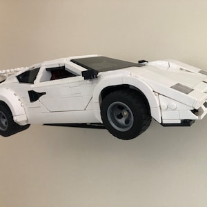 May include: A white Lego model of a Lamborghini Countach sports car. The car is built with small plastic bricks and has a detailed exterior.