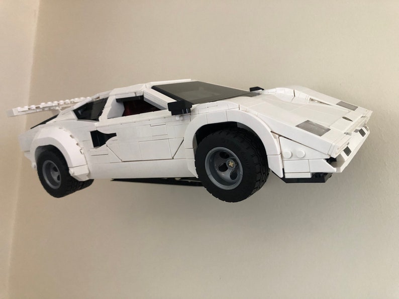May include: A white Lego model of a Lamborghini Countach sports car. The car is built with small plastic bricks and has a detailed exterior.