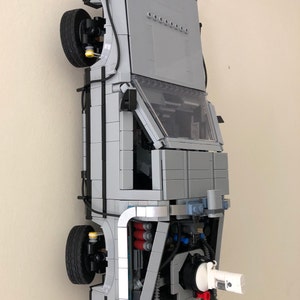 May include: A gray and silver Lego model of the DeLorean time machine from the Back to the Future movie. The model is built with intricate details, including the iconic gull-wing doors, the flux capacitor, and the engine.