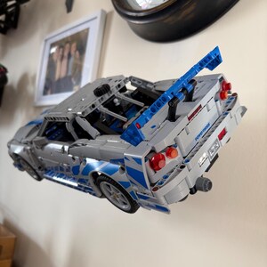 May include: A silver and blue toy car made of interlocking plastic bricks. The car has a spoiler, red taillights, and the text "TOYO TIRES" on the back. The car is angled, showing its side and rear details.