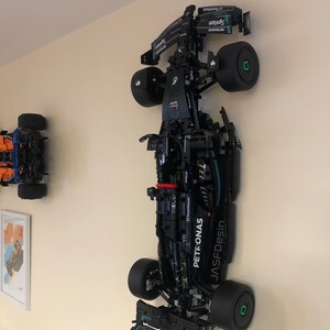 May include: A black and green Lego model of a Formula 1 race car with the Petronas logo on the side. The car is mounted on a wall.
