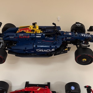 May include: A blue and yellow Lego Formula 1 race car with the Oracle and Red Bull logos. The car is on a white wall.