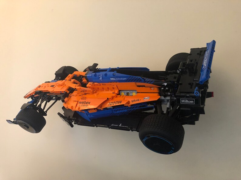 May include: A blue and orange Lego Formula 1 race car with various sponsors including Dell Technologies, Webex, Splunk, and Hilton.