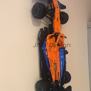 May include: A Lego McLaren Formula 1 race car model with orange and blue details. The car has sponsors' logos including 'Webex by Cisco', 'Mclaren', 'Dell Technologies', 'Splunk', and 'Hilton'.