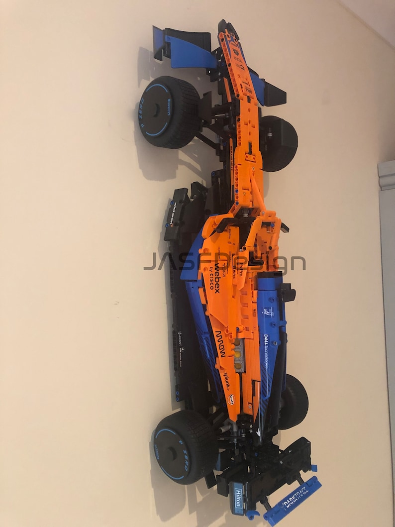 May include: A Lego McLaren Formula 1 race car model with orange and blue details. The car has sponsors' logos including 'Webex by Cisco', 'Mclaren', 'Dell Technologies', 'Splunk', and 'Hilton'.