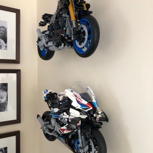 Peut inclure: Deux mod&egrave;les de moto Lego mont&eacute;s sur un mur. La moto du haut est noire avec des accents jaunes et des roues bleues. La moto du bas est blanche avec des accents bleus et rouges et des roues noires.