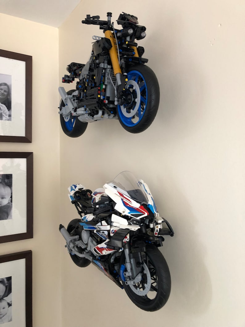 Peut inclure: Deux mod&egrave;les de moto Lego mont&eacute;s sur un mur. La moto du haut est noire avec des accents jaunes et des roues bleues. La moto du bas est blanche avec des accents bleus et rouges et des roues noires.