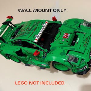 May include: Green Lego Porsche race car with red and white accents. The car has the word "PORSCHE" on the top and the number "77" on the side. The text "WALL MOUNT ONLY" and "LEGO NOT INCLUDED" are also visible.