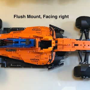 May include: A black and orange Lego McLaren Formula 1 race car with blue wings. The car has the words "webex by CISCO" and "MOWW" printed on the side. The car is in a flush mount position, facing right.