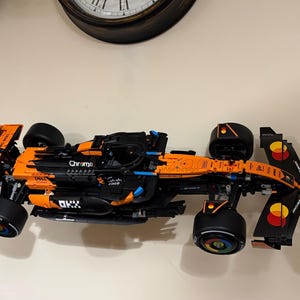 May include: A black and orange race car model with sponsor logos, including "Chrome" and "Dell." The model has large black tires and is set against a neutral background. The car's design is detailed, with visible mechanical components.