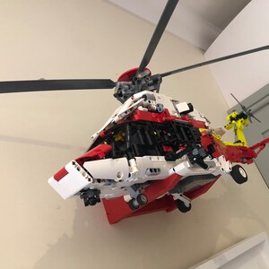 May include: A red, white, and yellow Lego helicopter model with a black rotor blade. The helicopter is mounted on a wall.