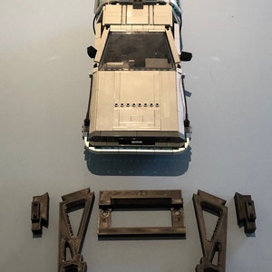 May include: A white Lego DeLorean time machine from the Back to the Future movie franchise. The car is on a blue surface with four gray Lego pieces beside it.