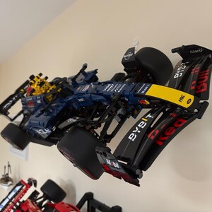 May include: A black and blue Lego Formula 1 race car with yellow and red accents. The car has the words "Red Bull" and "Bybit" on the side. The car is hanging on a wall.