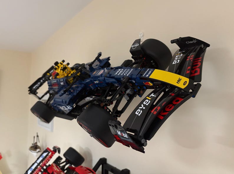 May include: A black and blue Lego Formula 1 race car with yellow and red accents. The car has the words "Red Bull" and "Bybit" on the side. The car is hanging on a wall.