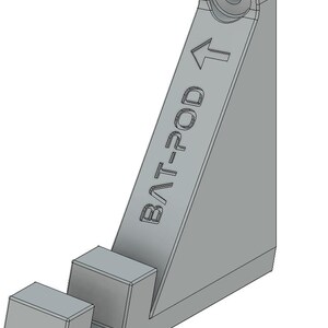 Op de afbeelding: Een grijze plastic wandbeugel met de tekst "BAT-POD" en een pijl die omhoog wijst. De beugel heeft een haak aan de onderkant om een object aan op te hangen.