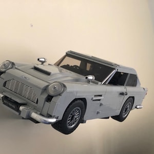 May include: A gray Lego model of the iconic Aston Martin DB5 sports car, featuring a detailed exterior and a black interior. The car is floating in mid-air, showcasing its intricate design.