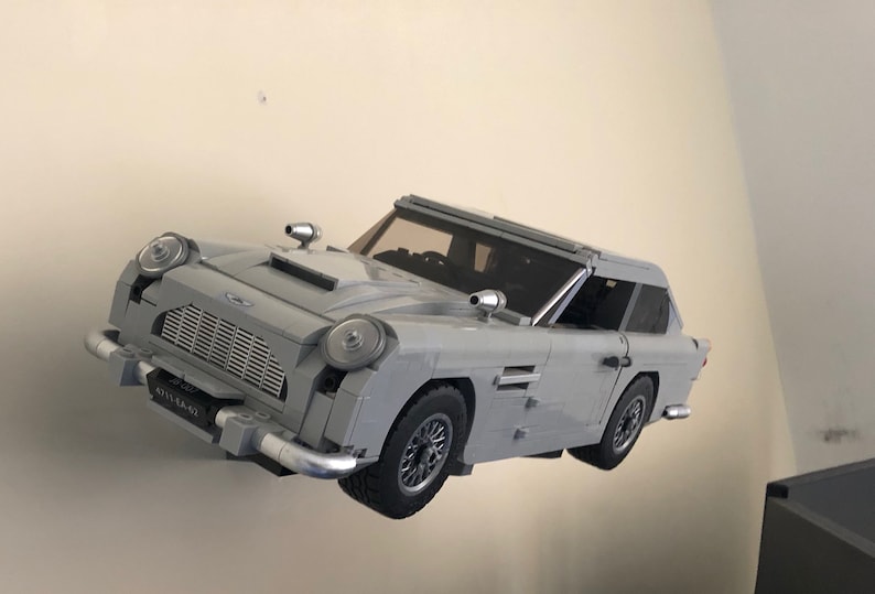May include: A gray Lego model of the iconic Aston Martin DB5 sports car, featuring a detailed exterior and a black interior. The car is floating in mid-air, showcasing its intricate design.