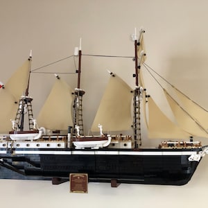 May include: A detailed model of a black and white sailing ship with brown masts and white sails. The ship is mounted on a wooden base and has a plaque with the word "Endurance" on it.