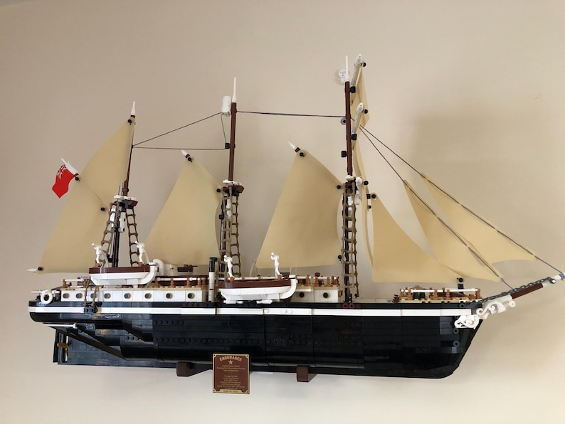 May include: A detailed model of a black and white sailing ship with brown masts and white sails. The ship is mounted on a wooden base and has a plaque with the word "Endurance" on it.