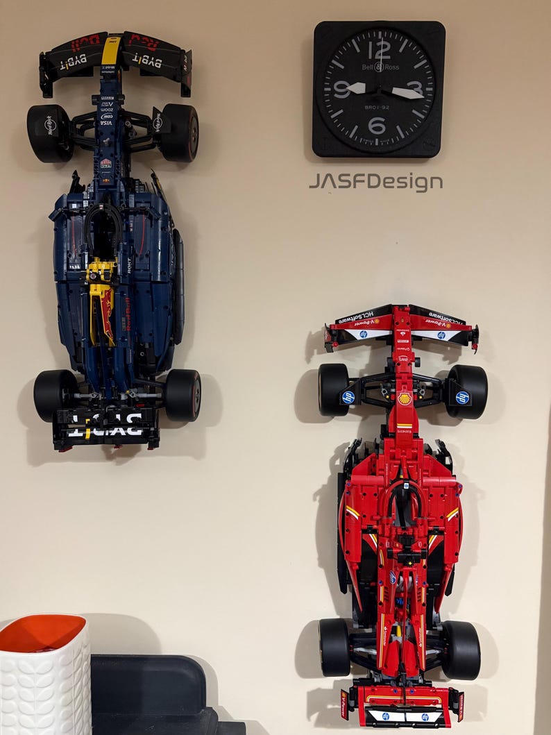 May include: Two Lego Formula 1 race cars mounted on a wall. The car on the left is blue and black with red accents and the car on the right is red with black and white accents. The cars are displayed upside down with the wheels facing the wall.