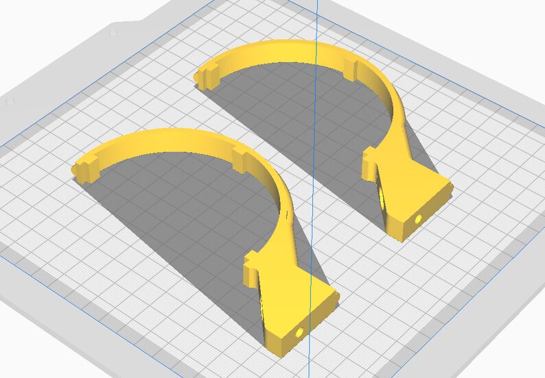 May include: Two yellow, semi-circular 3D-printed objects. Each piece has a flat base with a circular hole and a curved top with rectangular notches. The objects are set against a grid background, suggesting a design or modeling context.