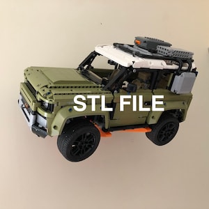 Puede incluir: Un modelo de SUV verde oliva y blanco con ruedas negras y baca. El texto "STL FILE" se muestra en blanco en el lateral del veh&iacute;culo. El modelo est&aacute; montado en una pared.