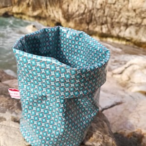 Könnte beinhalten: Ein blauer Stoffkorb mit einem geometrischen Muster aus weißen und orangefarbenen Quadraten. Der Korb ist zusammengefaltet und liegt auf einer felsigen Oberfläche. Der Text "Panier enduit 2" ist am unteren Rand des Bildes sichtbar.