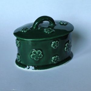 May include: A green ceramic trinket box with a floral design and a handle on the lid.