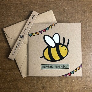 May include: A brown card with a yellow and black bee illustration and the text "Hap-Bee Birthday". The bee is flying with a string of colorful flags above it.