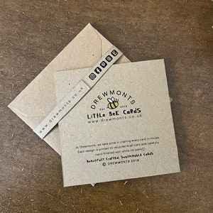 May include: A brown card with a bee logo and the text "Drewmonts Est 2019 Little Bee Cards www.drewmonts.co.uk". The card also includes the text "At Drewmonts, we take pride in crafting every card in-house. Each design is printed on recycled Kraft card and carefully hand-finished with white ink pens. Beautifully Crafted, Sustainable Cards &copy; Drewmonts 2019".