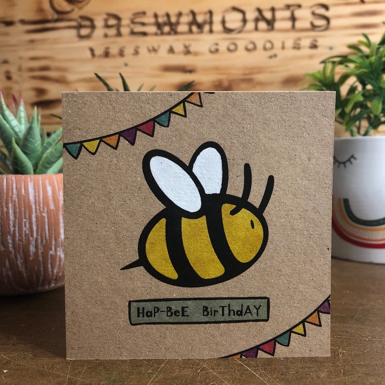 May include: A brown card with a yellow and black bee illustration and colorful pennant flags. The card says "Hap-Bee Birthday".
