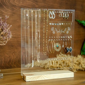 May include: A clear acrylic jewelry organizer with a wooden base. The organizer has slots for necklaces, earrings, and bracelets. It is a great way to keep your jewelry organized and easy to find.