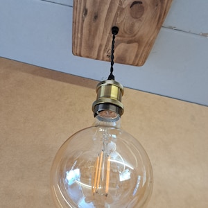 May include: A clear glass globe light bulb with a gold metal socket and a black cord hanging from a wooden ceiling fixture.