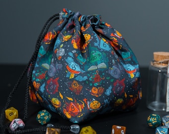 May include: A dark fabric drawstring bag featuring a colorful pattern of multi-sided gaming dice, open books, and flames. The bag is cinched with black braided cords and is surrounded by several loose polyhedral dice and a small glass jar.