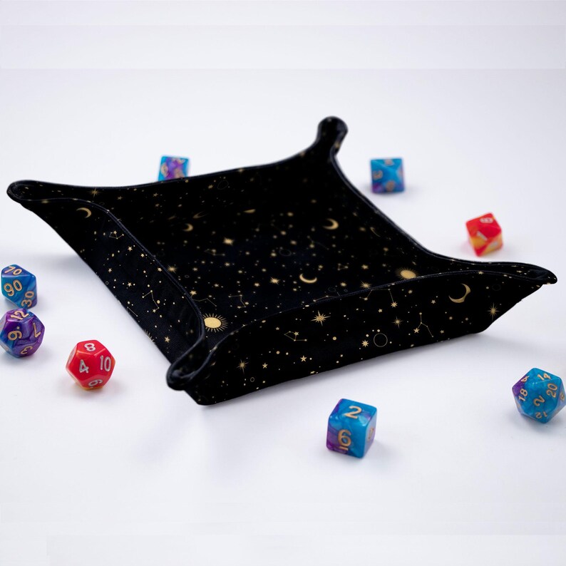 May include: A black velvet dice tray with a gold constellation pattern. The tray is filled with colorful dice.