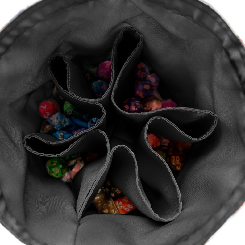 May include: A dark gray fabric dice bag with a circular opening and internal dividers creating six distinct compartments. Each section is filled with a variety of multi-colored polyhedral dice featuring different numbers and patterns.
